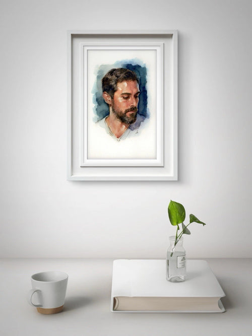 Black-and-white watercolor painting of a seated male figure with blue hands, framed by white mat board against light wall.